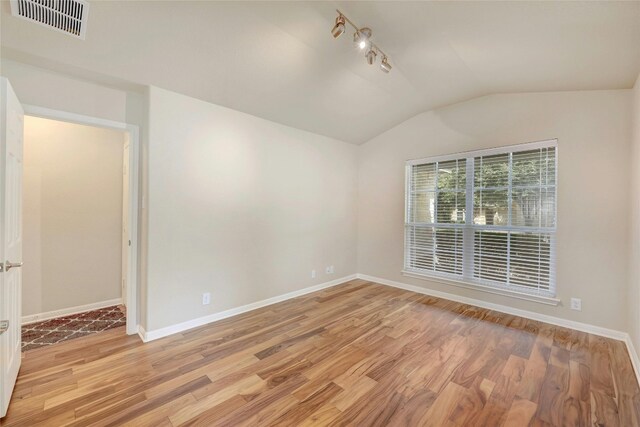 spare room featuring vaulted ceiling, track lighting, and light hardwood / wood-style floors