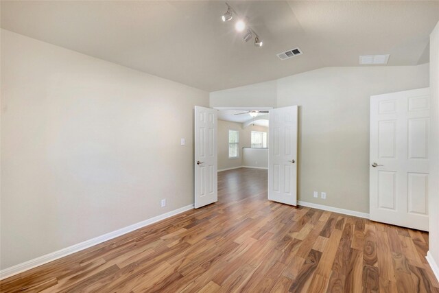 unfurnished bedroom featuring wood-type flooring, lofted ceiling, and rail lighting