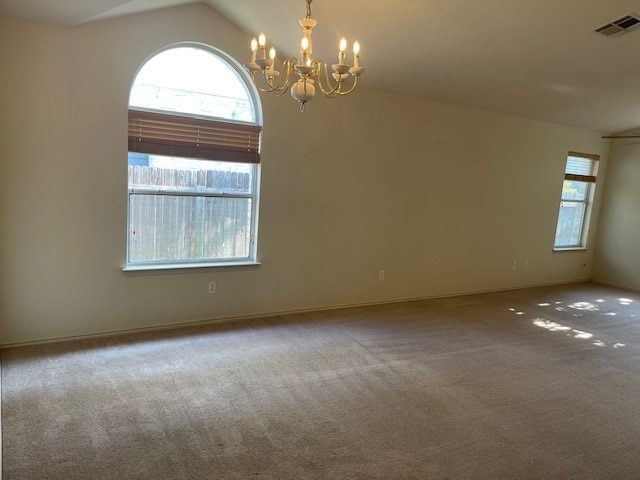 carpeted empty room with vaulted ceiling and a chandelier