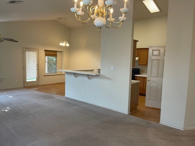 kitchen with hanging light fixtures, ceiling fan with notable chandelier, high vaulted ceiling, light carpet, and a breakfast bar area