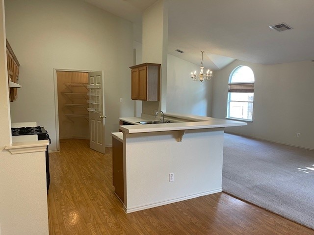 kitchen featuring an inviting chandelier, sink, pendant lighting, kitchen peninsula, and light colored carpet