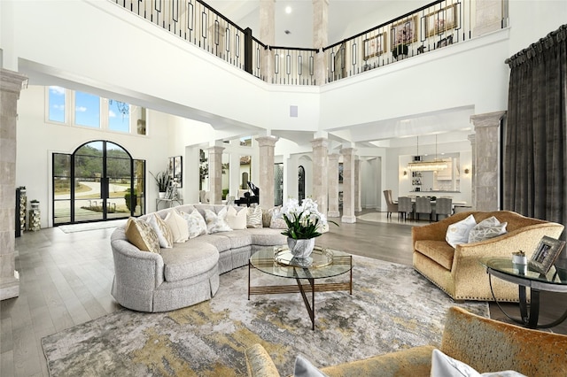 living room featuring hardwood / wood-style flooring, a towering ceiling, and decorative columns