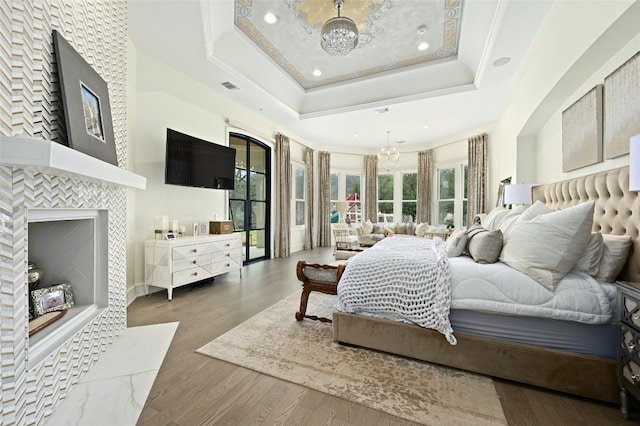 bedroom featuring a raised ceiling, a tiled fireplace, dark wood-type flooring, and a chandelier