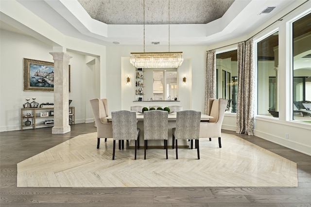 dining area with a raised ceiling, a notable chandelier, and ornate columns