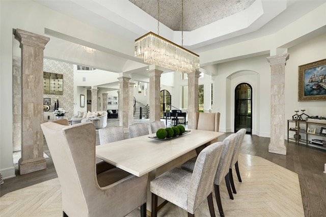 dining area with a tray ceiling, parquet flooring, a high ceiling, and ornate columns