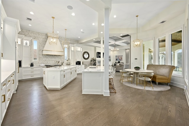 kitchen with hanging light fixtures, an island with sink, white cabinets, and custom range hood