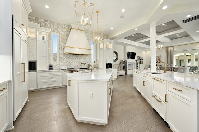 kitchen with premium range hood, pendant lighting, an inviting chandelier, and a large island with sink