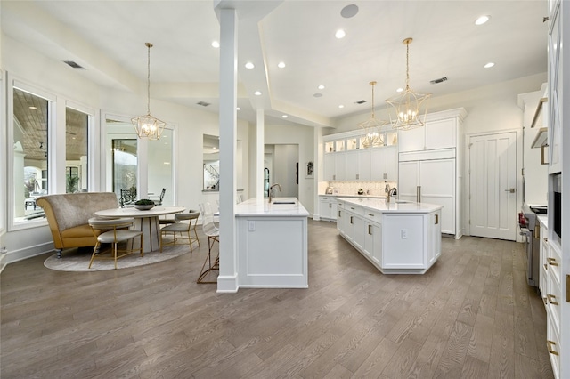 kitchen featuring pendant lighting, sink, white cabinets, a center island with sink, and an inviting chandelier