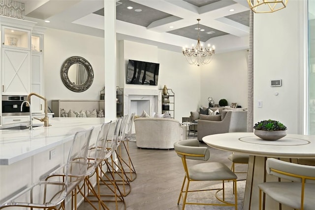 dining space with sink, beam ceiling, coffered ceiling, light hardwood / wood-style floors, and a chandelier