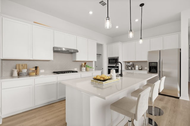 kitchen with stainless steel appliances, pendant lighting, a center island with sink, light hardwood / wood-style floors, and white cabinetry