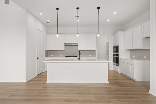 kitchen with stainless steel oven, white cabinetry, an island with sink, and hanging light fixtures