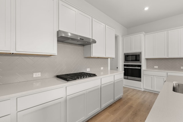 kitchen with light hardwood / wood-style floors, white cabinets, exhaust hood, and appliances with stainless steel finishes