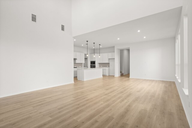 unfurnished living room with light hardwood / wood-style flooring and a towering ceiling