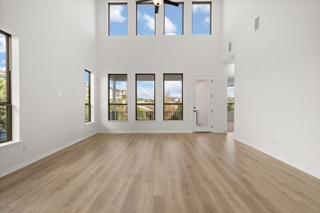 unfurnished living room with ceiling fan, a towering ceiling, and light hardwood / wood-style floors