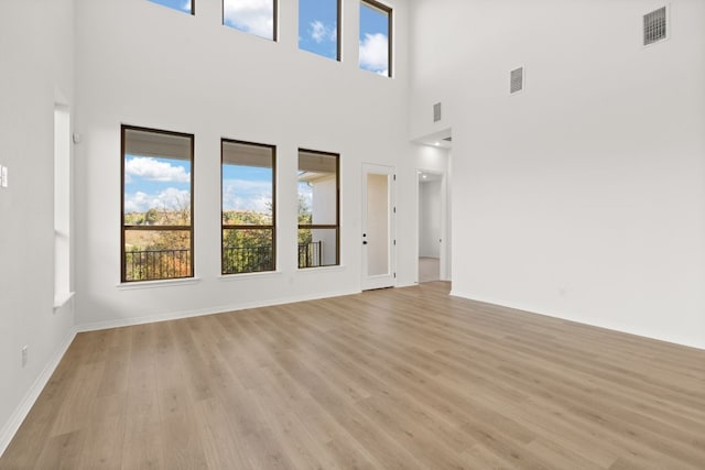 unfurnished living room featuring a high ceiling and light hardwood / wood-style flooring