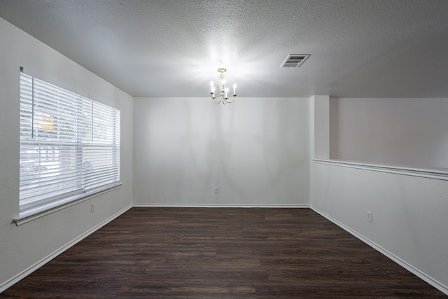 spare room with a textured ceiling, dark hardwood / wood-style flooring, and a chandelier