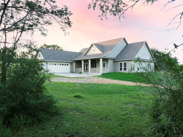 back house at dusk featuring a garage, a lawn, and covered porch