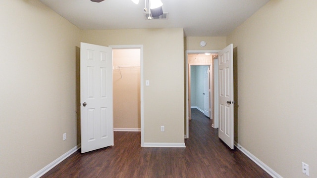 unfurnished bedroom featuring a walk in closet, a closet, ceiling fan, and dark hardwood / wood-style floors