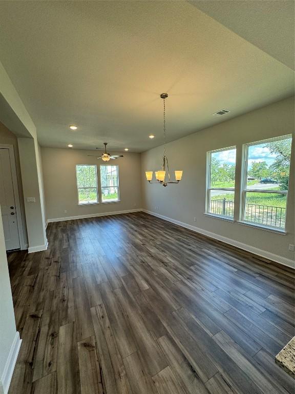 unfurnished dining area with baseboards, visible vents, dark wood-style flooring, and ceiling fan with notable chandelier