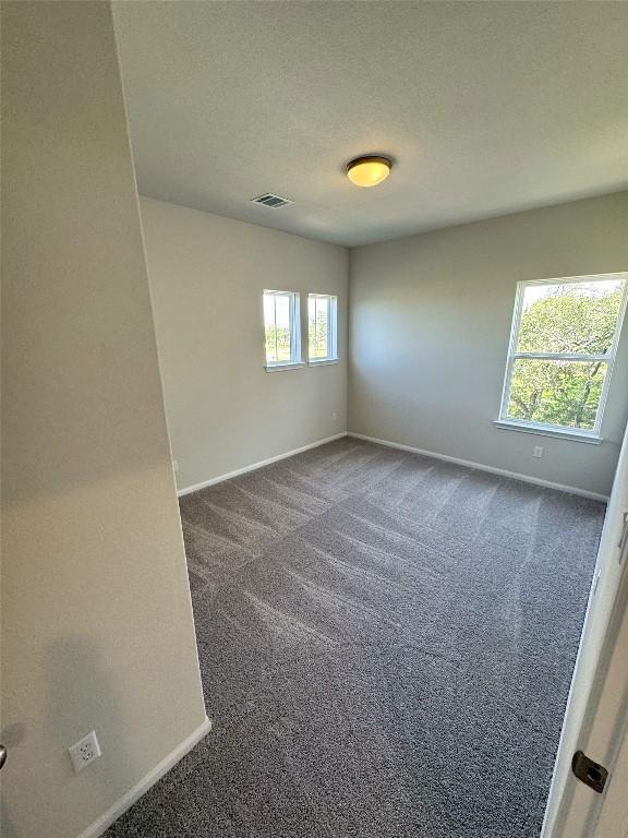 spare room with visible vents, dark carpet, a textured ceiling, and baseboards