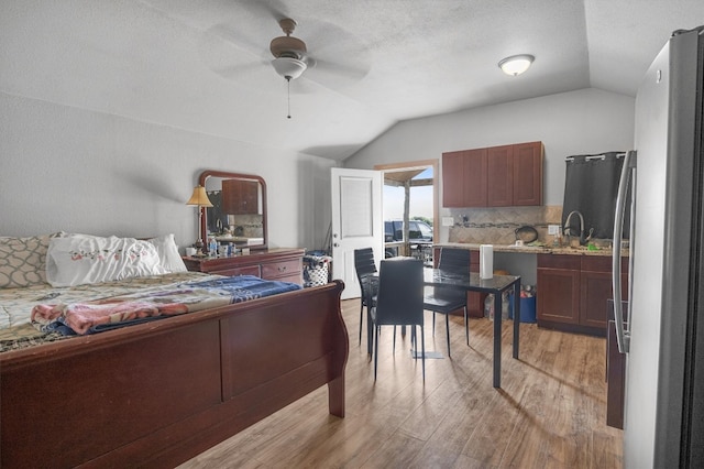 bedroom with light wood-type flooring, a textured ceiling, ceiling fan, vaulted ceiling, and sink