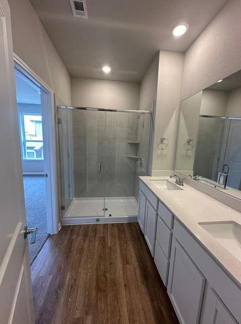 bathroom with a shower with shower door, hardwood / wood-style floors, and dual bowl vanity