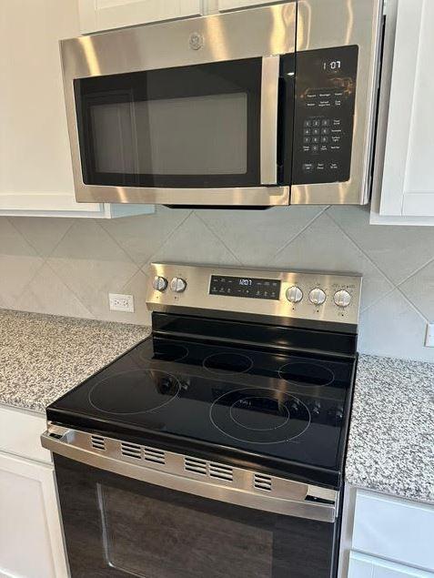 kitchen featuring appliances with stainless steel finishes, white cabinets, decorative backsplash, and light stone countertops