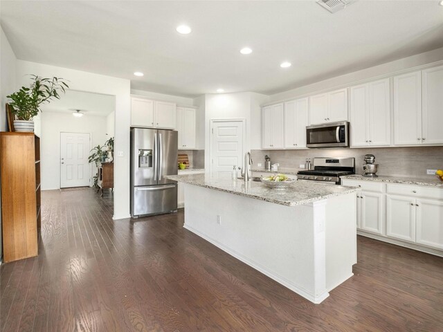 kitchen with appliances with stainless steel finishes, tasteful backsplash, white cabinets, an island with sink, and dark wood-type flooring