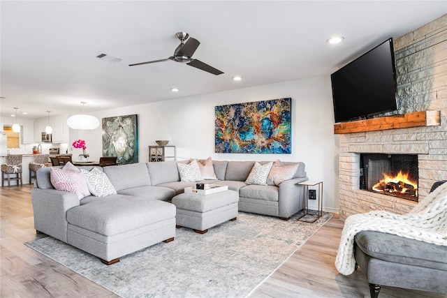 living room featuring a stone fireplace, light hardwood / wood-style flooring, and ceiling fan