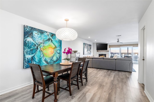 dining area with ceiling fan, a fireplace, and light hardwood / wood-style flooring