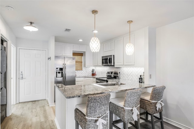 kitchen with stainless steel appliances, kitchen peninsula, hanging light fixtures, and white cabinets