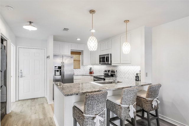 kitchen featuring light stone counters, a peninsula, appliances with stainless steel finishes, white cabinetry, and tasteful backsplash