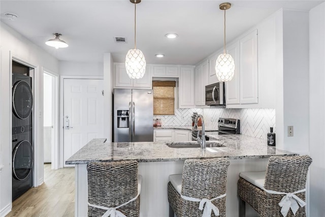 kitchen featuring backsplash, stacked washer and dryer, appliances with stainless steel finishes, a peninsula, and a sink