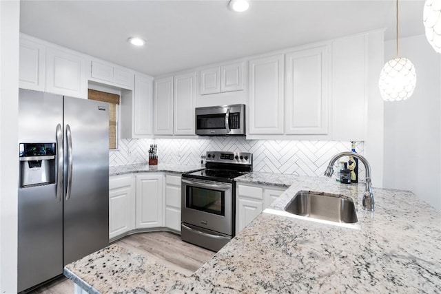 kitchen with white cabinets, light stone countertops, stainless steel appliances, and a sink