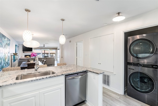 kitchen with white cabinetry, sink, hanging light fixtures, stacked washer / drying machine, and stainless steel dishwasher