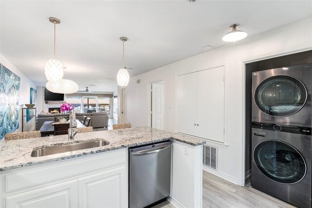 kitchen featuring light stone countertops, stainless steel dishwasher, white cabinets, stacked washer / drying machine, and a sink