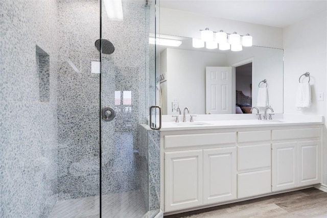 ensuite bathroom featuring a sink, wood finished floors, a stall shower, and double vanity