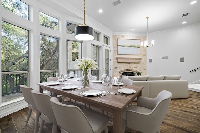 dining room with dark wood-type flooring, ornamental molding, a fireplace, and a notable chandelier