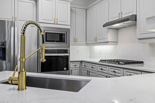 kitchen with sink, stainless steel appliances, tasteful backsplash, light stone counters, and white cabinets