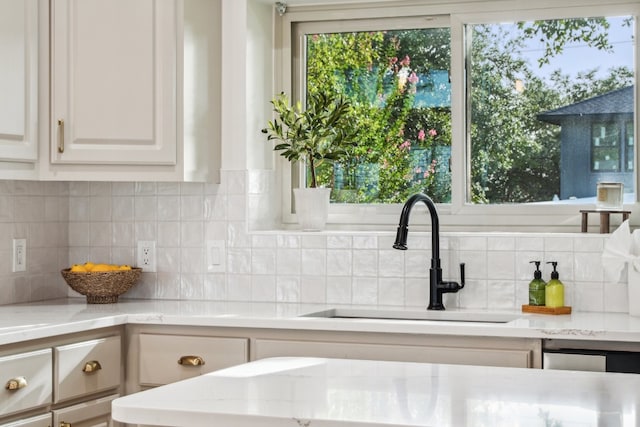 kitchen with white cabinetry, decorative backsplash, sink, and light stone counters