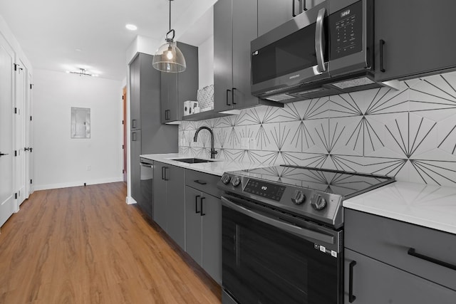 kitchen with decorative light fixtures, stainless steel appliances, decorative backsplash, light wood-type flooring, and sink