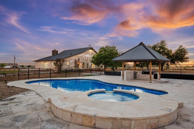 pool at dusk with an in ground hot tub, a gazebo, and a patio area