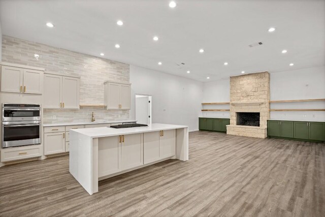 14409 Bois D Arc Ln, Manor, TX 78653 - kitchen with light wood-type flooring, a large island, stainless steel double oven, a fireplace, and light countertops
