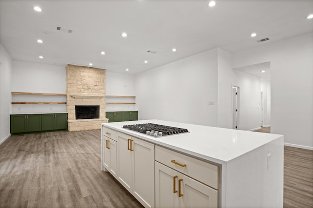 kitchen featuring light hardwood / wood-style flooring, stainless steel gas stovetop, white cabinets, a center island, and a fireplace