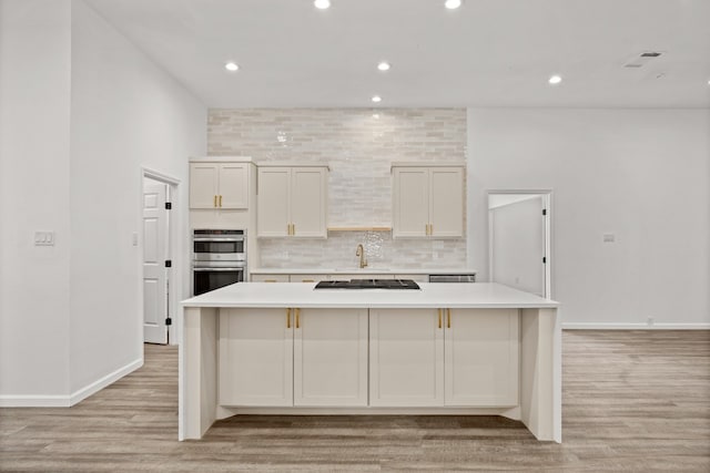 kitchen featuring decorative backsplash, a kitchen island, light wood-type flooring, and double oven