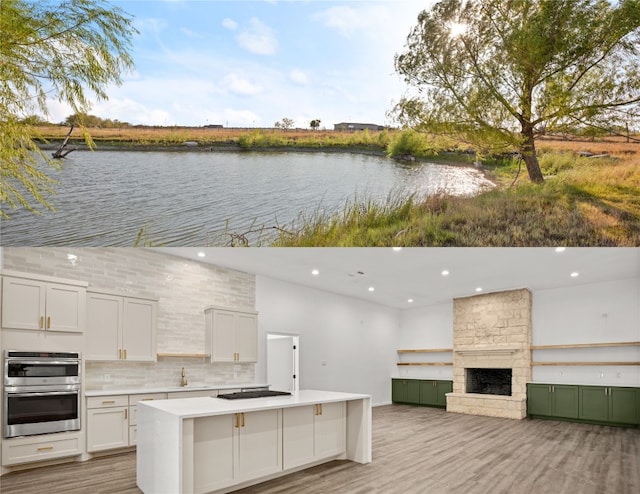 exterior space with white cabinetry, an outdoor stone fireplace, a water view, stainless steel double oven, and light hardwood / wood-style flooring