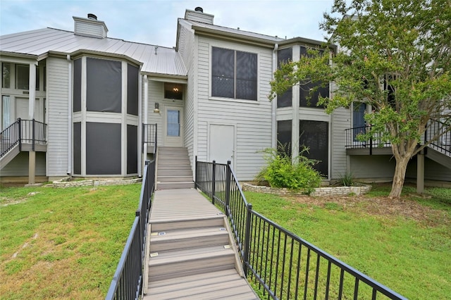 back of property featuring stairs, metal roof, a chimney, and a lawn