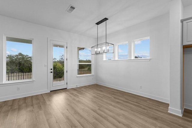 unfurnished dining area featuring light hardwood / wood-style floors, an inviting chandelier, and a healthy amount of sunlight