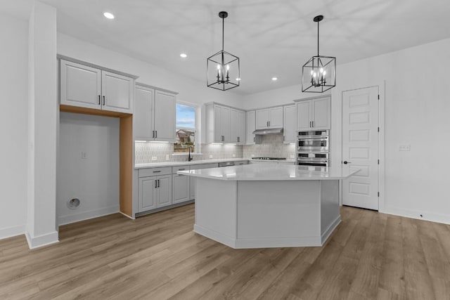 kitchen featuring pendant lighting, a center island, stainless steel double oven, and light wood-type flooring