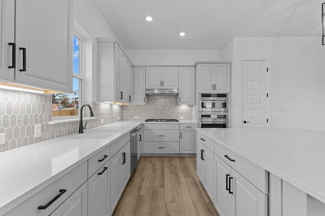 kitchen featuring decorative backsplash, stainless steel appliances, sink, light hardwood / wood-style flooring, and white cabinets